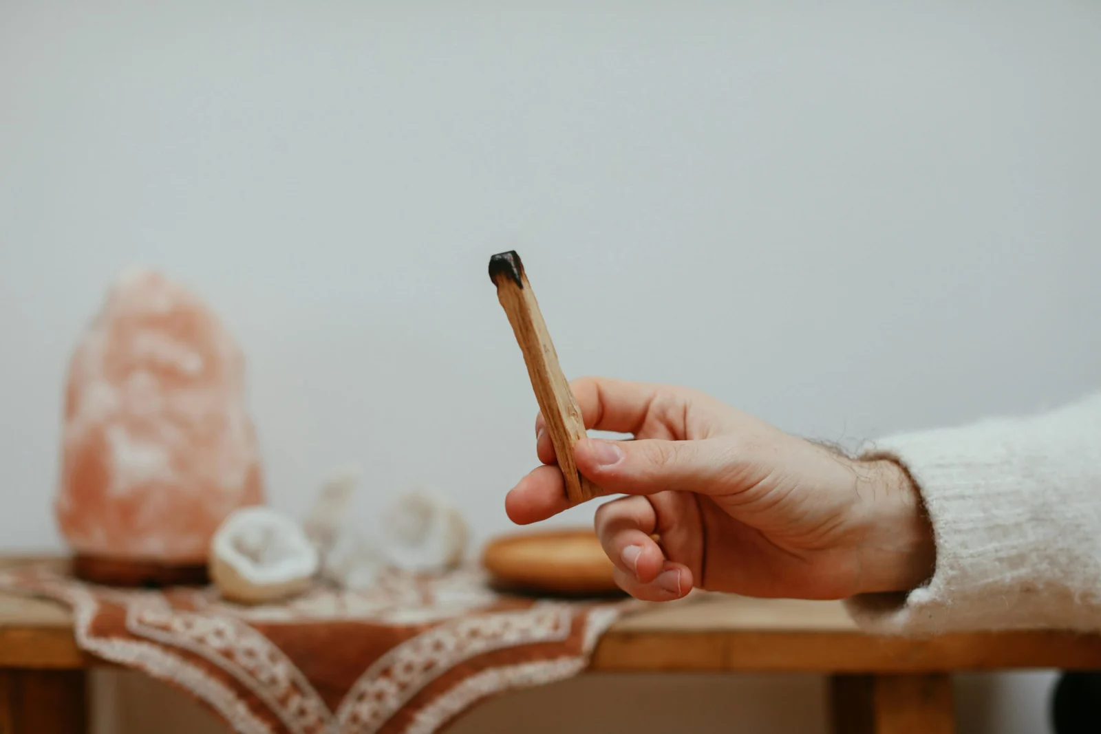 Een hand met een houten geurstaafje boven een tafel